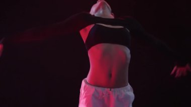 Bir kız büyüleyici bir zarafet ve cazibeyle kırmızı stüdyo ışıklarının gizemli atmosferinde karanlık bir arkaplanda dans eder.