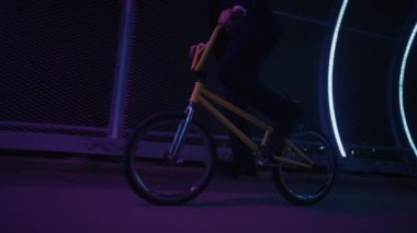 Becerikli bir BMX sürücüsü burun manüel numaraları ustalığını sergiliyor, gece vakti neon ışıklarıyla zincirleme tünelde sorunsuzca geziniyor.