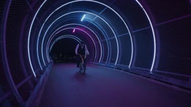 Bir BMX sürücüsü, gece vakti neon ışıklarıyla bir yaya köprüsünde kusursuz bir ön taklayla yerçekimine meydan okur.