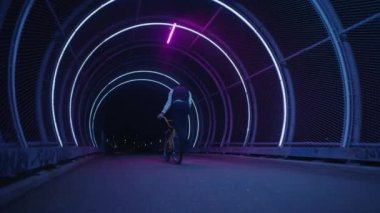 Sokak süvarileri, neon ışıklarla dolu bir yaya köprüsünde, gecenin arkaplanına karşı bağırsak kaldırma hareketleri sergiliyor.