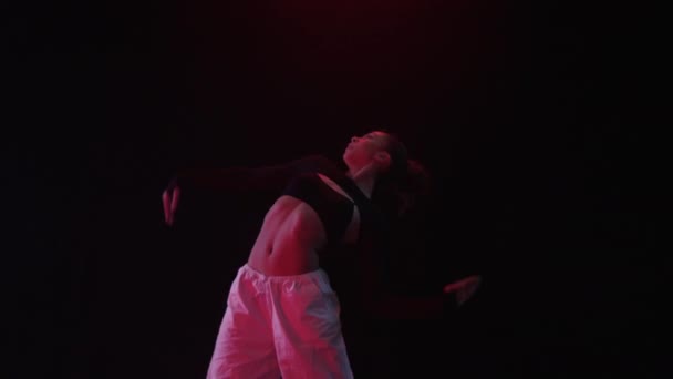 一个女孩优雅地在一个黑色的工作室背景下跳舞 沐浴在柔和的红色光芒中 免版税图库视频