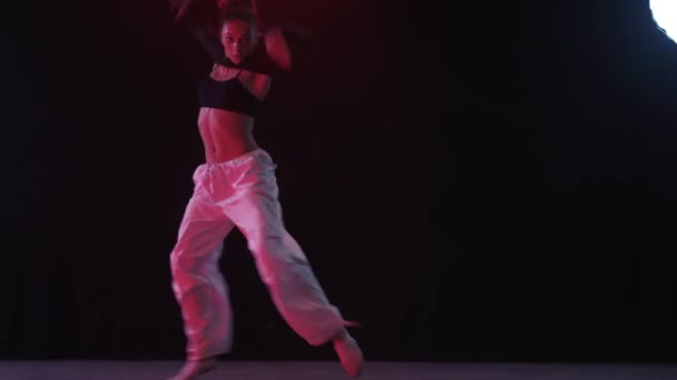 柔軟な女の子は微妙な赤いライトによって照らされた黒いスタジオの背景に対して魅惑的なダンスを行います ストック映像