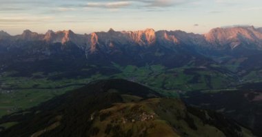 Sabah güneşinin yumuşak parıltısıyla yıkanan bir dağ silsilesinin çarpıcı drone görüntüsü. Işığın ve gölgenin karmaşık etkileşimi görkemli tepeleri ve yemyeşil vadileri vurgular.