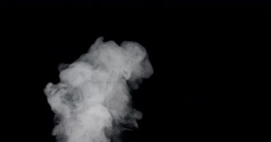 Yoğun, beyaz duman bulutlarının yavaş çekim görüntüsü yükseliyor. Koyu arkaplan dumanın desenlerini ve hareketlerini vurguluyor