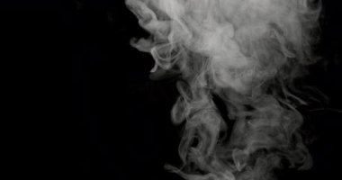 Karanlık bir arka plana yayılan ve dağılan bir duman. Soyut desenleri ve hareketleri yavaş çekimde parlak ışıkla aydınlatılır.