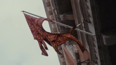 Venedik 'in görkemli kırmızı ve altın bayrağını gündüz vakti gökyüzüne karşı bir balkonda gösteren alçak açılı çekim.