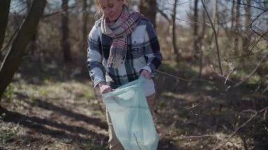 A tracking shot of a dedicated woman collecting trash amidst the tranquility of nature