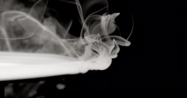 Zarif bir şekilde yükselen ve kıvrılan dumanlardan oluşan yakın plan karanlık bir arka planda sıvı kıvrılır. Işık dumanı ve karanlık zemin arasındaki zıtlık