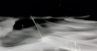 Karanlık bir yüzey boyunca sürüklenen dumanın yakın çekim görüntüsü. Duman ince ve ruhani görünür, ince dallar ve daha kalın dalgalar birbirine karışır.