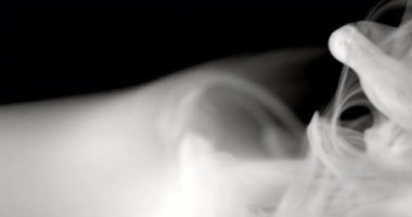 Siyah bir yüzeyden yakın plan duman üfleniyor. Duman zarif bir şekilde yüzeye yayılıyor ve yayılıyor.