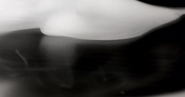 Siyah bir yüzey üzerinde dinamik ve akışkan hareketini gösteren yakın plan bir duman. Duman ince ve ruhani görünür. Değişen yoğunluklar ve girdaplar soyut bir desen oluşturur.