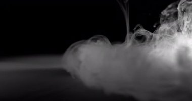 Bir duman bulutu yere iner ve düz bir yüzeye yayılır. Duman yoğun ve dalgalı görünüyor, karmaşık girdap ve desenlerle. Sahnedeki ışıklandırma sigara şeklini ve dokusunu vurguluyor.