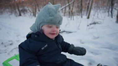 Kıkırdayan bir bebek kışlık giysiler içinde neşeli bir şekilde kızağa biniyor.