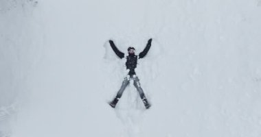 Kışlık giysiler içindeki bir adam kar altında sırt üstü yatar, bir kar meleği yaratmak için sevinçle kollarını ve bacaklarını hareket ettirir. Etrafına kar taneleri yavaşça yağar ve sakin kış atmosferine katılır.