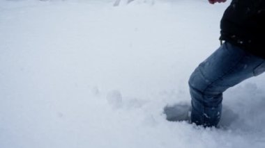 Botlar ve kotlar giyen bir adamın karlı arazide güçlü adımlarla yürüdüğü, kışın kasıtlı adımlarla yol alırken el değmemiş karda derin izler bıraktığı bir yakın plan.