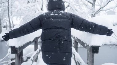 Bir adam kollarını, sakin bir göle bakan karlı bir tırabzanda kaydırmaktan zevk alır. Kış cazibesiyle göldeki sükuneti birleştirir.