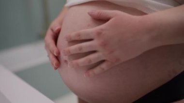 Hamile bir kadının karnını dikkatlice okşarken yakın plan görüntüsü.