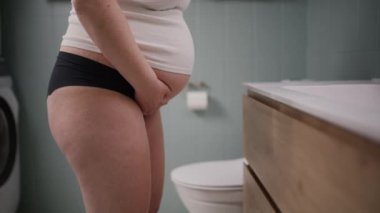 Yakın çekim, hamile bir kadının banyo ortamında rahatsızlığını hissederken karnını ve bacaklarını yakalar.