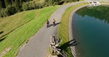 İki bisikletçi, dingin yemyeşil bir göl boyunca pedal çeviriyor.