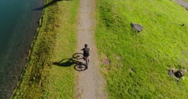 Bir bisikletçi, bereketli yeşilliklerle çevrili görkemli göl yolu boyunca sakin bir yolculuktan zevk alır.