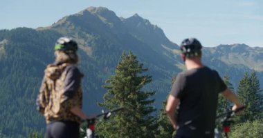 Bisikletçiler, manzaralı dağ manzaralı ve yemyeşil manzaralı bisikletleriyle sohbete daldılar, sakin ve resimsel bir ortam yarattılar.