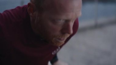 Açık havada dalış egzersizi yapan kararlı bir adamın yakın çekim görüntüsü. Yüzü bulanık kentsel bir arkaplan karşısında oluşan konsantrasyon ve çabayı gösteriyor.