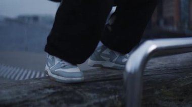 Bir adam, şehir rıhtımındaki ahşap bir bankta yüksek yoğunluklu bir idmanı şehir binaları ve su zeminine karşı sergiliyor.