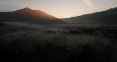 İnsansız hava aracı, sakin, sisli, görkemli dağ siluetlerinin arasına kurulmuş, gün doğumunun yumuşak renklerinde yıkanmış bir kasabayı ortaya çıkarıyor.