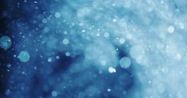 Parlak, ağırlıklı olarak mavi parçacıklar kıvrılır ve karanlık bir arkaplanda hareket eder. Parçacıklar boyutları ve yoğunlukları farklılık göstererek dinamik bir hareket hissi yaratıyor.