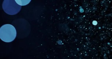 Bir dizi mavi parçacık karanlık bir arkaplanda yüzüyor. Parçacıkların değişen boyutları daha büyük ve daha tanımlı olan katmanlı bir etki yaratır.,