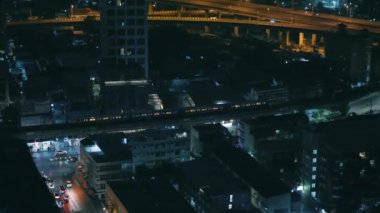 Aydınlatılmış binaların ve caddelerin yanından arabayla geçen bir tren, karanlık çöktükten sonra hareket halindeki şehir yaşamını büyüleyici bir şekilde gösteriyor.