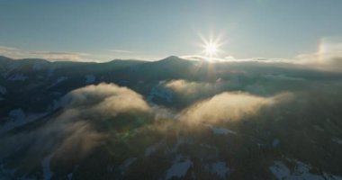 Güneşin sıcacık parıltısıyla yıkanan karlı dağların kuş bakışı görüntüsü.