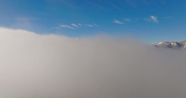 Karlı dağların tepeleri bulutların üzerinde yükseliyor, bir dronun yükselen perspektifinden çekiliyor.