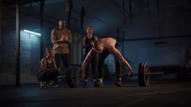 Bir grup hevesli CrossFitters azimli bir adam, hassas ve güç ile bir kapma kaldırma performans tezahürat yaparken, bir spor salonu içinde halter üzerinde tek bir hareket