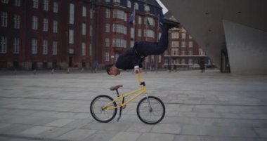 Takım elbise ve kravat giyen yetenekli bir BMX sürücüsü Nykredit Crystal binasına karşı kusursuz bir cesaret gösterisi sergiliyor.