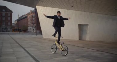 Takım elbiseli ve kravatlı bir BMX sürücüsü Kopenhag 'daki Nykredit Kristal Binası yakınlarında etkileyici numaralar yapıyor.