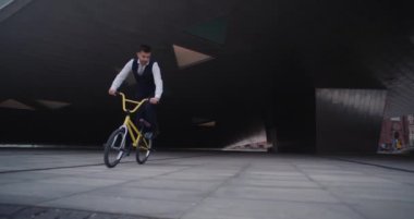 Yelekli ve kravatlı yetenekli bir BMX sürücüsü heyecan verici şehir sporlarında kusursuz bir tek teker dönüşü, hassasiyeti ve dengeyi ortaya koyuyor.