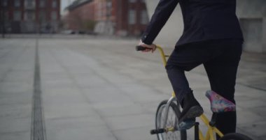 İş kıyafetli BMX sürücüsü takla atıyor ve el sallıyor.