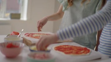 Ev yapımı pizzayla kaynaşan iki arkadaşın hamurlarına peynir serptiği keyifli bir sahne.