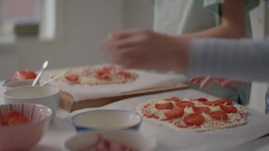 Mutfak tezgahında iki kız, pizza hamurlarına neşe içinde pepperoni dilimleri ekliyor, her parçayı dikkatlice yerleştirirken gülüyor ve sohbet ediyorlar, birlikte lezzetli ev yapımı pizzalar yapıyorlar.