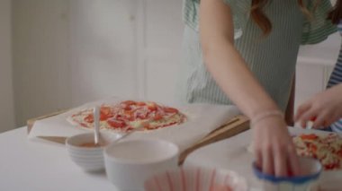 İki arkadaş, taze, canlı sebzelerle süslenmiş lezzetli bir ev yapımı pizza hazırlıyor. Sıcak bir mutfak ortamında birlikte yemek pişirmenin eğlenceli ve arkadaşça yönlerini sergiliyorlar.