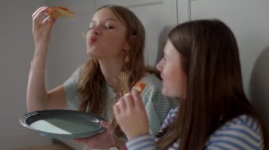 İki kız, lezzetli pizza dilimleri üzerinde kahkahalarını ve canlı sohbetlerini paylaşarak, birbirlerinin arkadaşlığından ve ortak bir yemeğin basit zevkinden zevk alırlarken, samimiyet ve dostluk atmosferi yaratıyorlar.