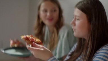 Bir grup kadın bir masanın etrafında toplanmış pizzanın tadını birlikte çıkarırken kahkaha ve keyif paylaşıyorlar, canlı ve neşeli bir arkadaşlık ve dostluk ortamı yaratıyorlar..