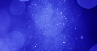 Mavi arka planda dönen beyaz bokeh parçacıkları kar tanelerini andırıyor.
