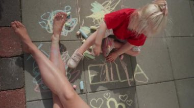 Bir çocuğun renkli tebeşirle adını yazıp, yaratıcılığını ve eğlenceli keşiflerini gösterdiği yüksek açılı bir fotoğraf.