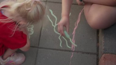 Bir anne ve çocuk yaratıcı tebeşir sanatı üzerine bağ kurar, beton bir yüzeyde neşeyle bir araya gelirler.