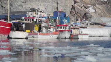 Kayıklar buzlu bir marinada huzur içinde dinleniyor engebeli, kayalık bir zemin ve mavi konteynır kamyonlarıyla kış manzarasına endüstriyel bir dokunuş ekleniyor.