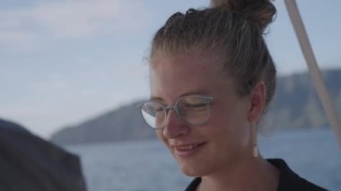 Sarışın bir kadının yakın plan fotoğrafı. Saçları bağlanmış, gözlük takıyor. Bir küpe de görünür. Kadın bir teknede dizüstü bilgisayarı üzerinde çalışıyor.
