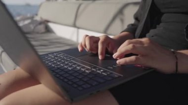 Laptop klavyesine yazı yazan bir kadının yakın plan fotoğrafı. Dizüstü bilgisayar kucağına konur ve o bir teknede oturur.