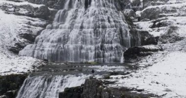 İnsansız hava aracı, heybetli Dynjandi Şelalesi 'ni bir kaya uçurumundan seyreden bir adama doğru uçuyor. Şelalenin huşu uyandıran manzarasını ve çağlayan suyun doğal güzelliğini emiyor.